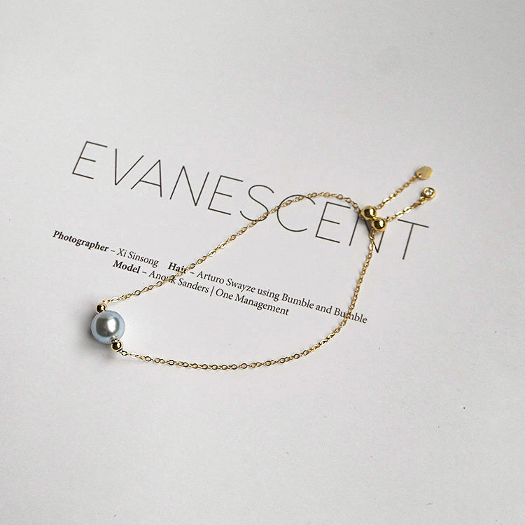 Gold bracelet with a silver bead on a light gray background, featuring the brand 'Evanescent'.