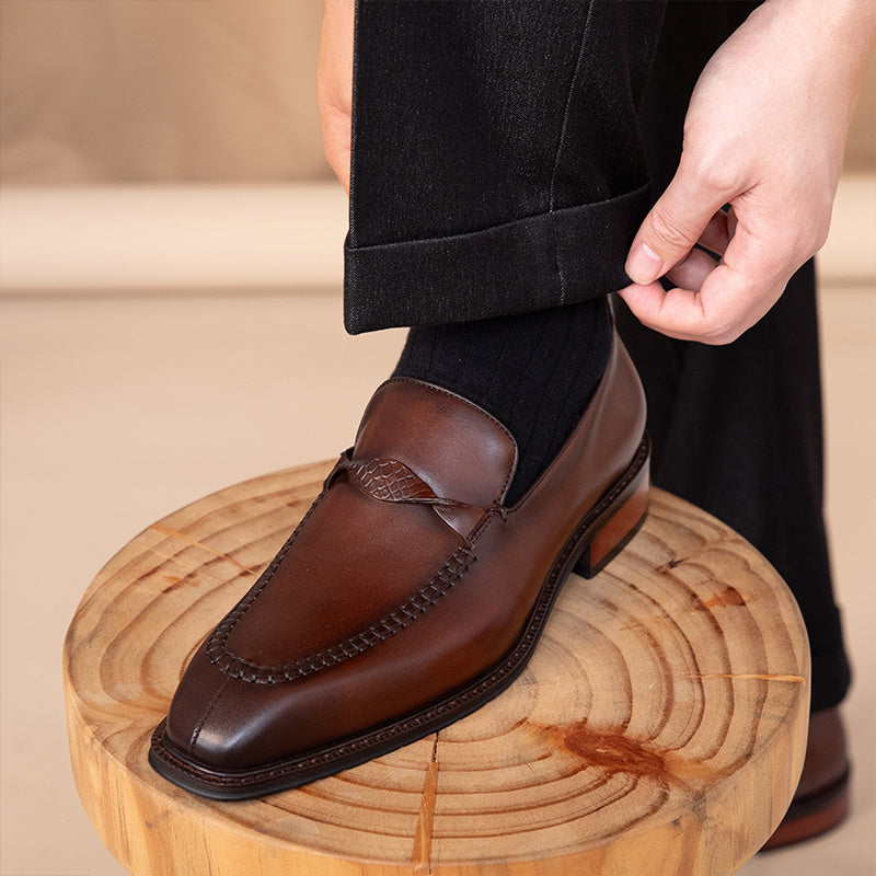 Brown leather loafer worn by a person on a wooden block with a beige background