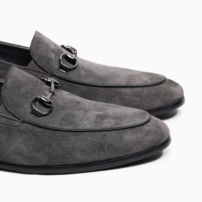 Gray suede loafers with decorative buckles on a white background