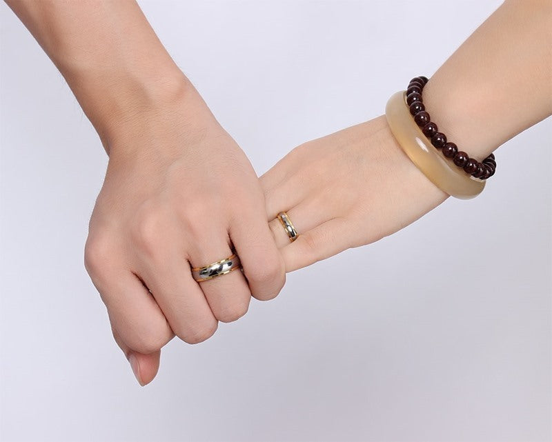 Two hands with gold rings on a plain background