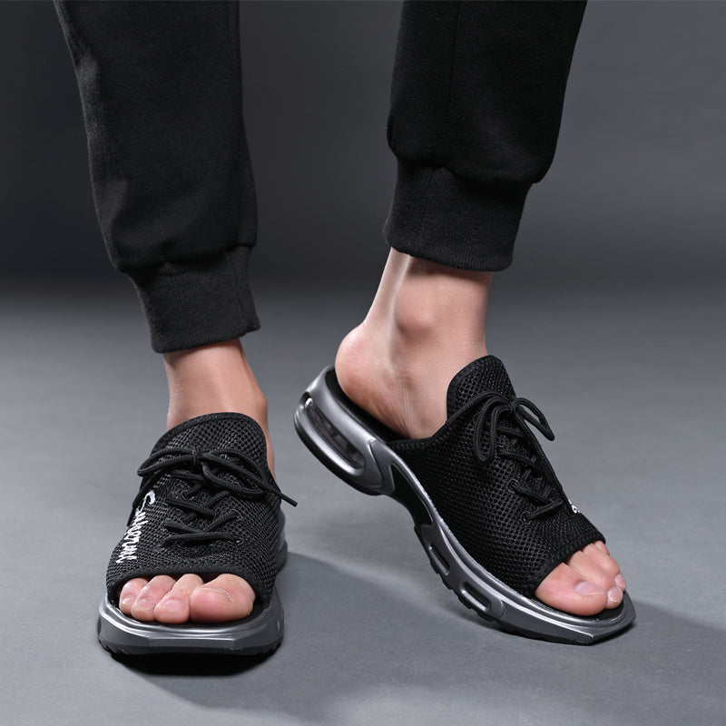 Black open-toe shoes worn with black pants on a gray background