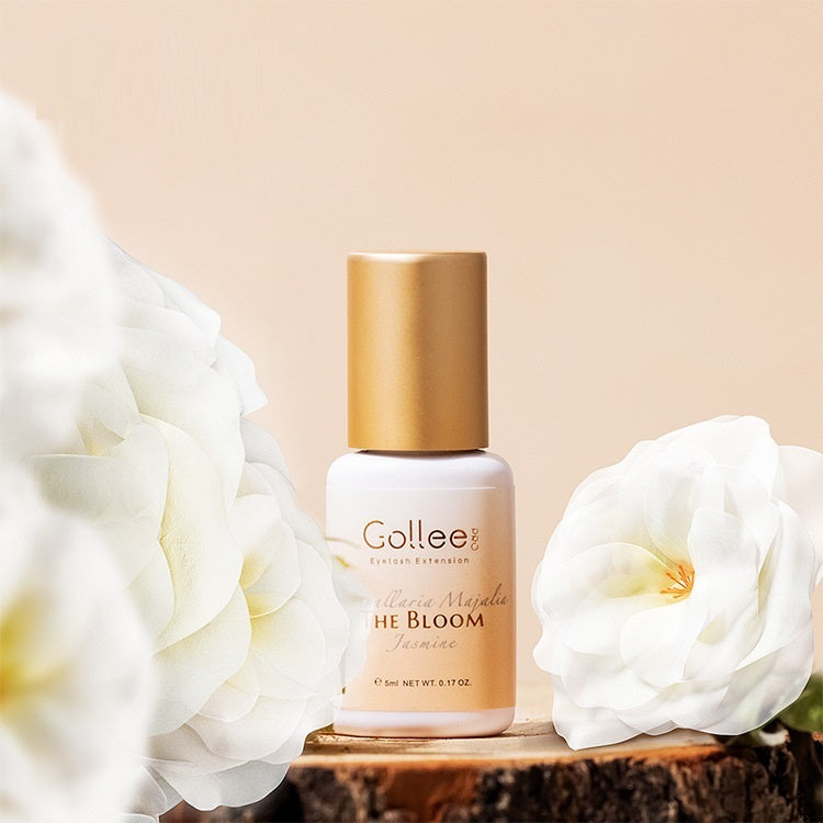 Gollee nail polish bottle with gold cap on a wooden surface surrounded by white flowers