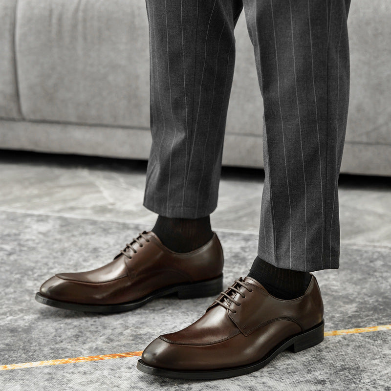 Brown leather shoes worn with gray pinstripe pants on a neutral background
