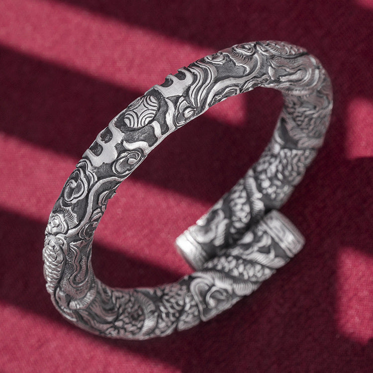Silver bracelet with intricate patterns on a red fabric background
