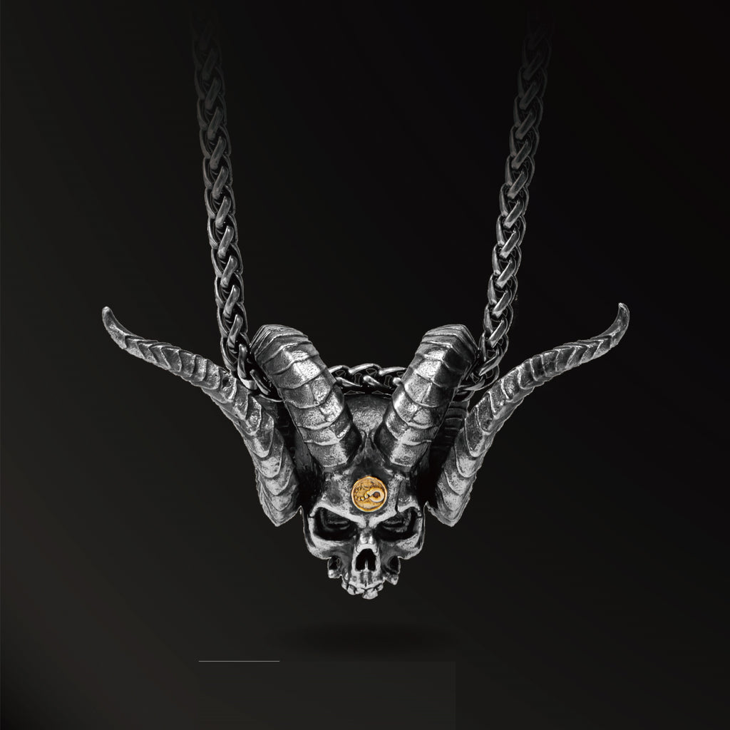 Skull pendant with goat horns and a gold eye on a black background