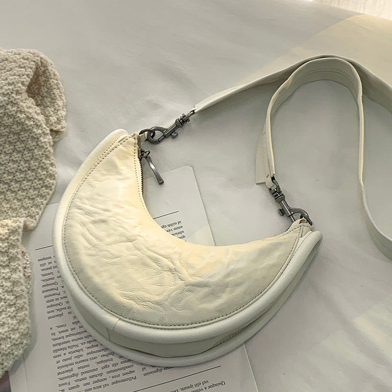 White crescent-shaped bag with a strap on a light surface