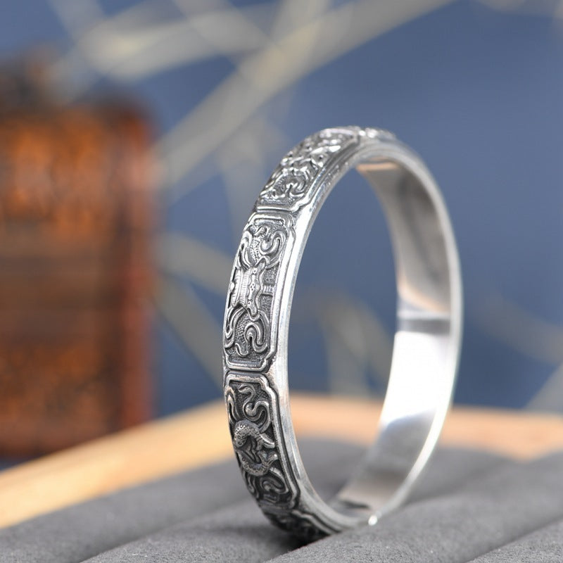 Silver bracelet with intricate designs on a textured surface with a blurred background