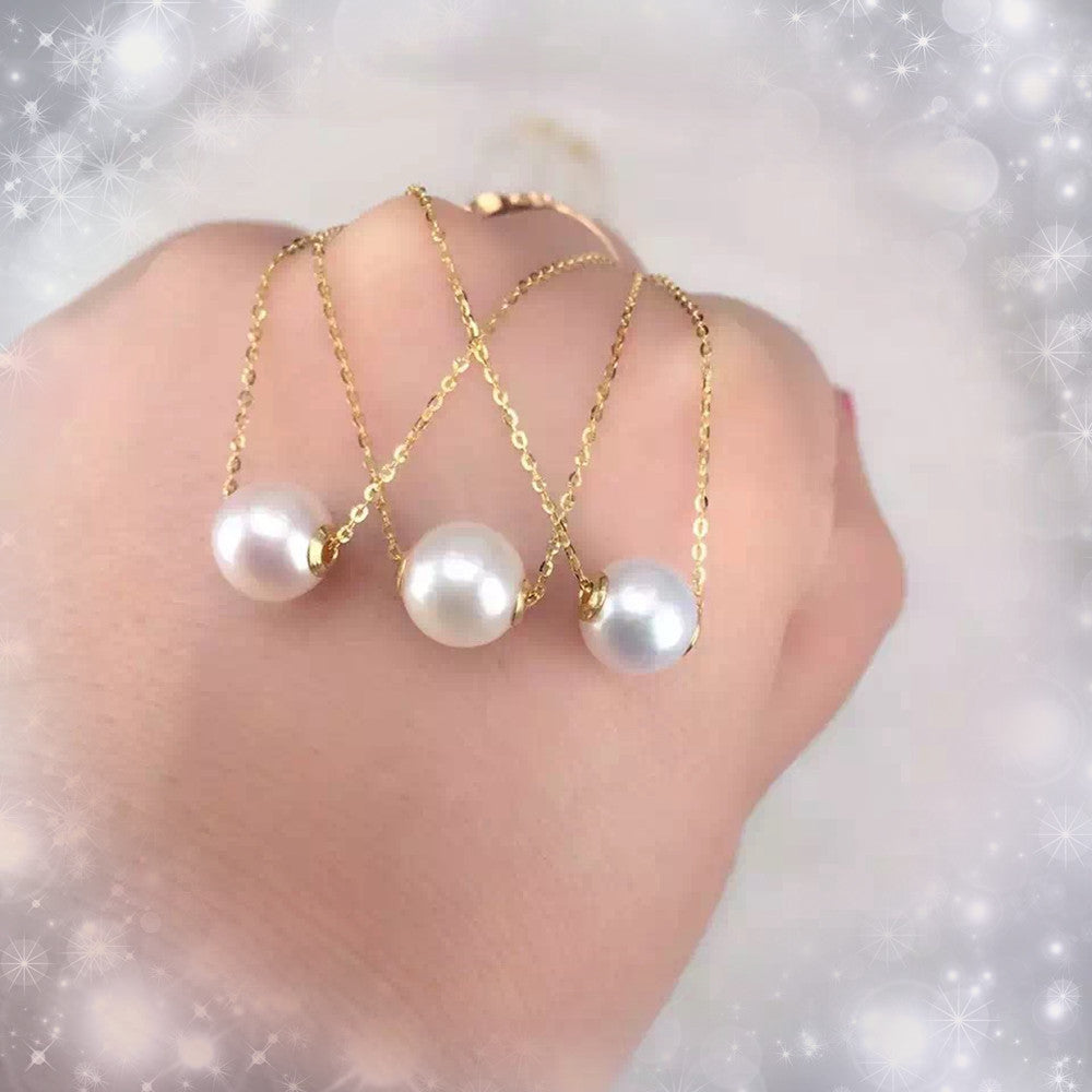 Three pearl necklaces on gold chains held by a hand against a soft, blurred background.