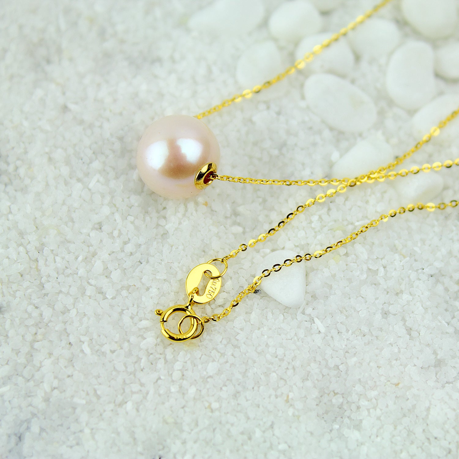 Gold necklace with a pink pearl pendant on a textured white surface