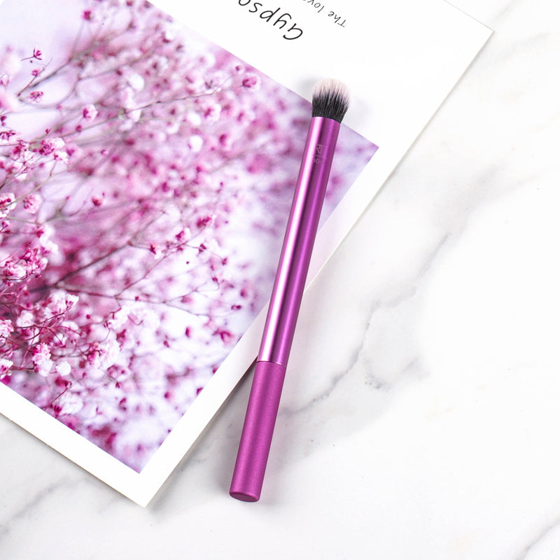 Purple makeup brush on a white surface with a pink floral background