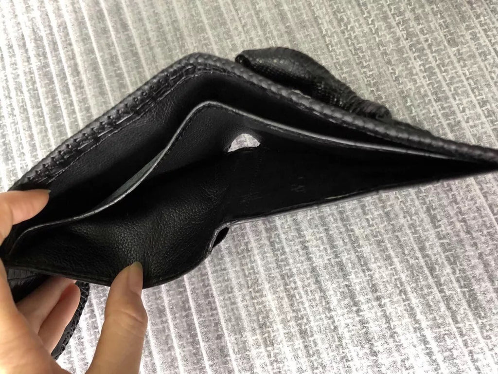 Black leather wallet held by a hand on a textured gray background