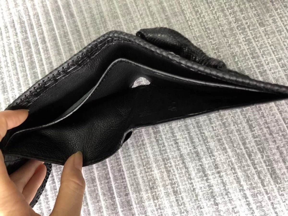 Black leather wallet held by a hand on a textured gray background