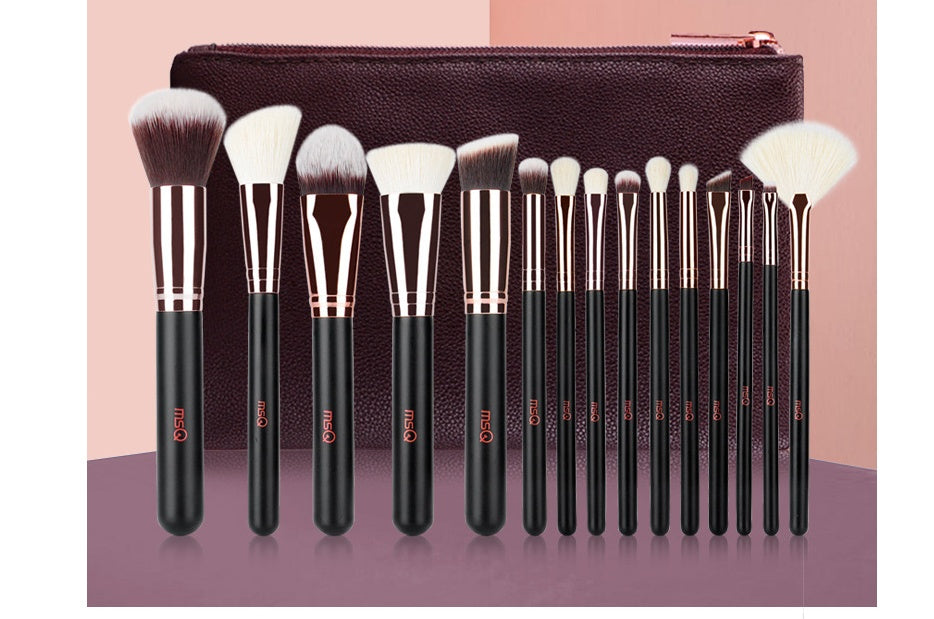 Set of makeup brushes with black handles and rose gold accents, displayed in front of a brown pouch on a pink and purple gradient background.