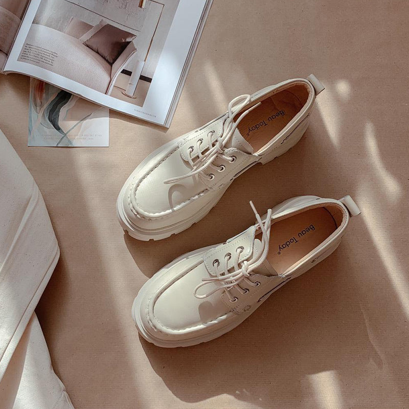 Pair of white sneakers on a beige surface with a magazine in the background