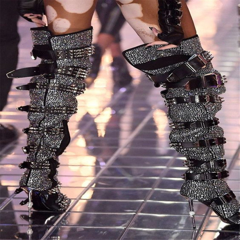 Decorative high-heeled boots with embellishments on a reflective floor.