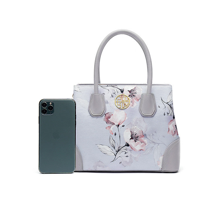 Floral-patterned handbag with a phone next to it on a white background