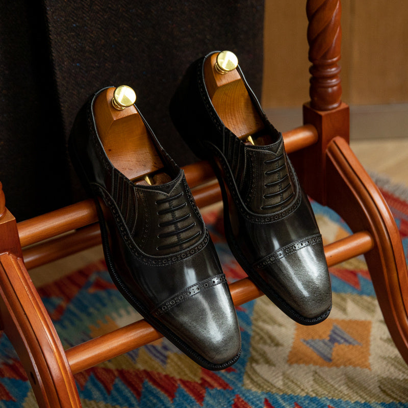 Pair of black dress shoes on a wooden chair with a colorful rug below.