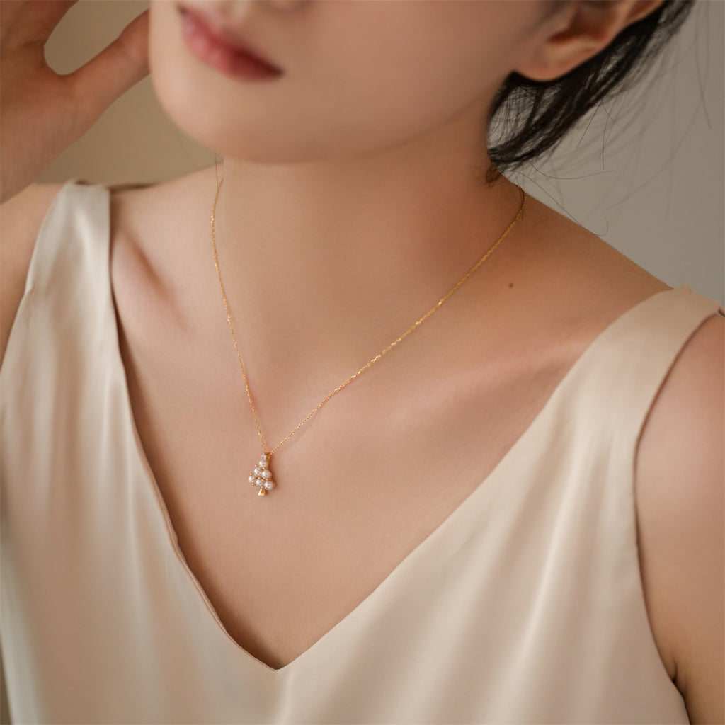 Woman wearing a delicate gold necklace with a small pendant against a neutral background