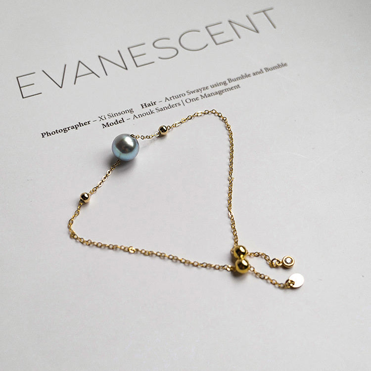 Gold bracelet with a single pearl on a light gray background with 'Evanescent' branding.