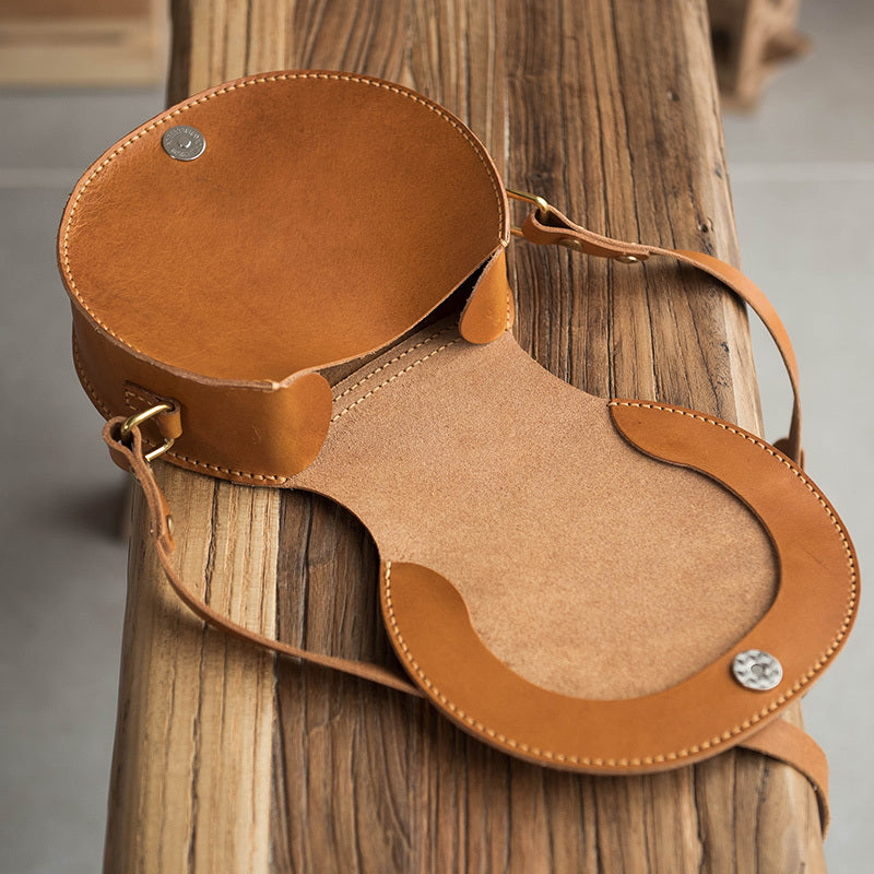 Brown leather bag with a strap on a wooden surface