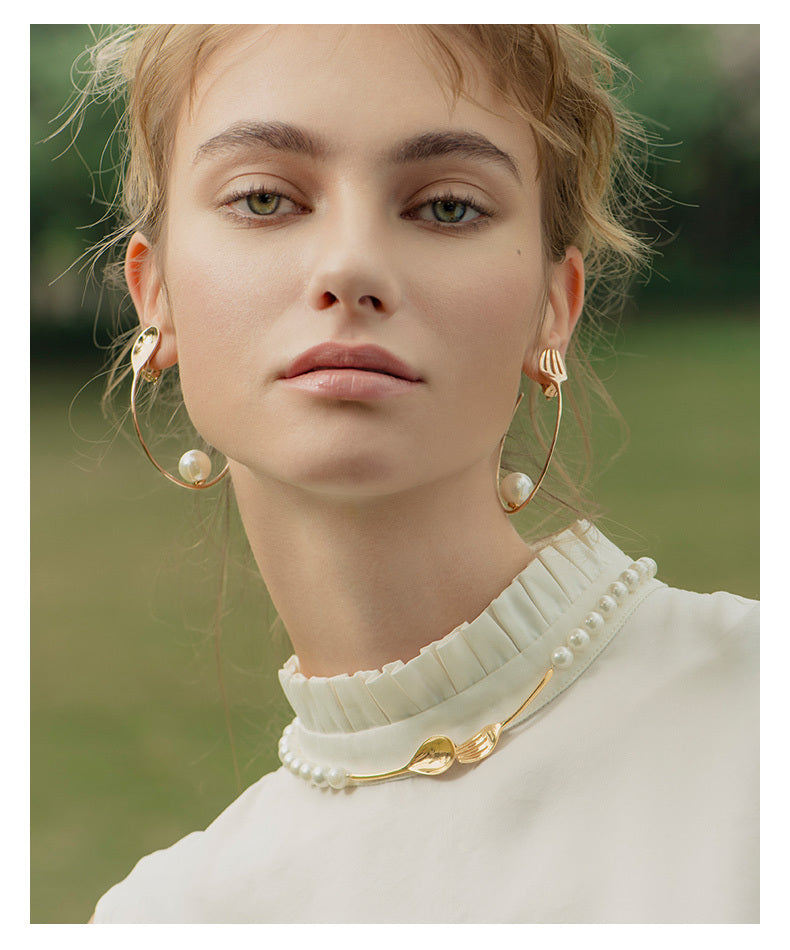 Woman wearing gold hoop earrings and a white top with pearl details.