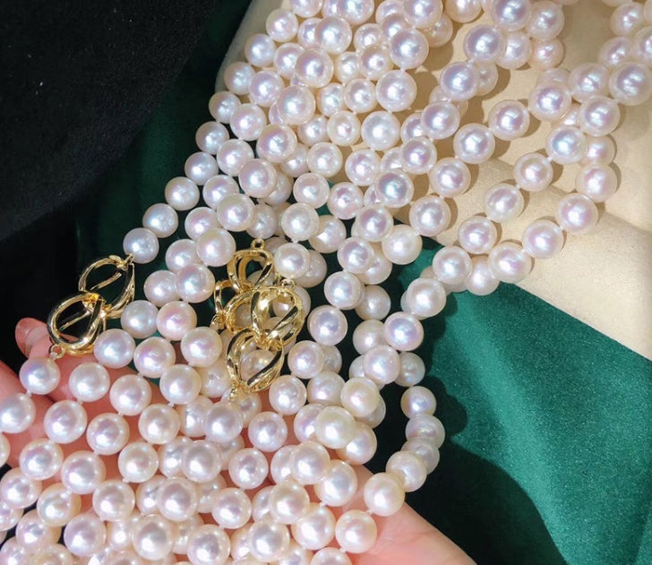 Pearl necklace with a gold clasp on a hand against a green and beige background