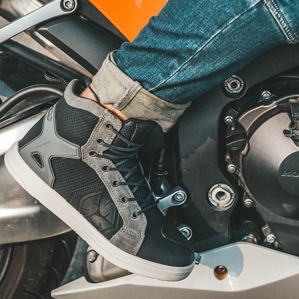 Person wearing black and gray motorcycle boots on a motorcycle.