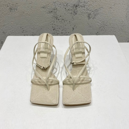 Pair of beige high-heeled sandals on a white surface with a gray textured background