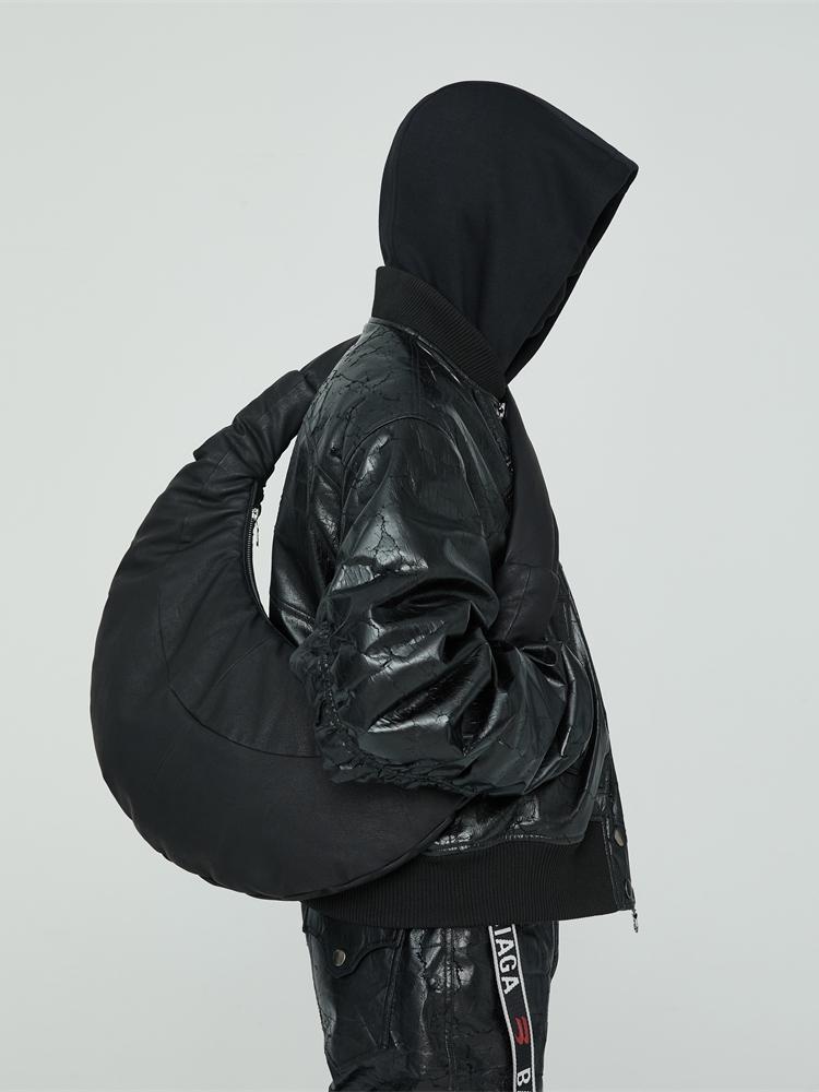 Person wearing a black hooded jacket with a reflective surface on a light gray background