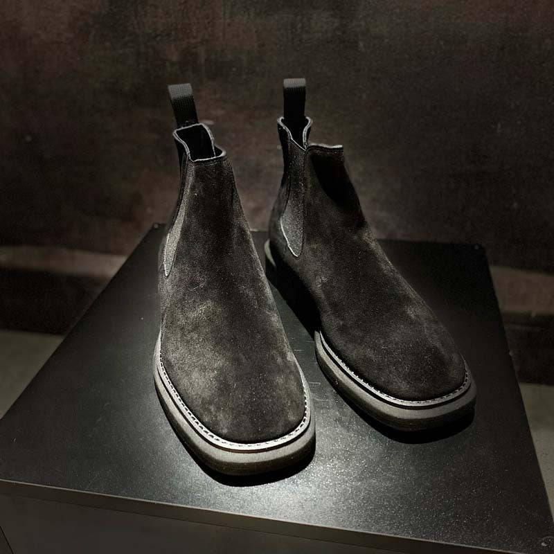 Pair of dark gray suede Chelsea boots on a black surface with a dark background