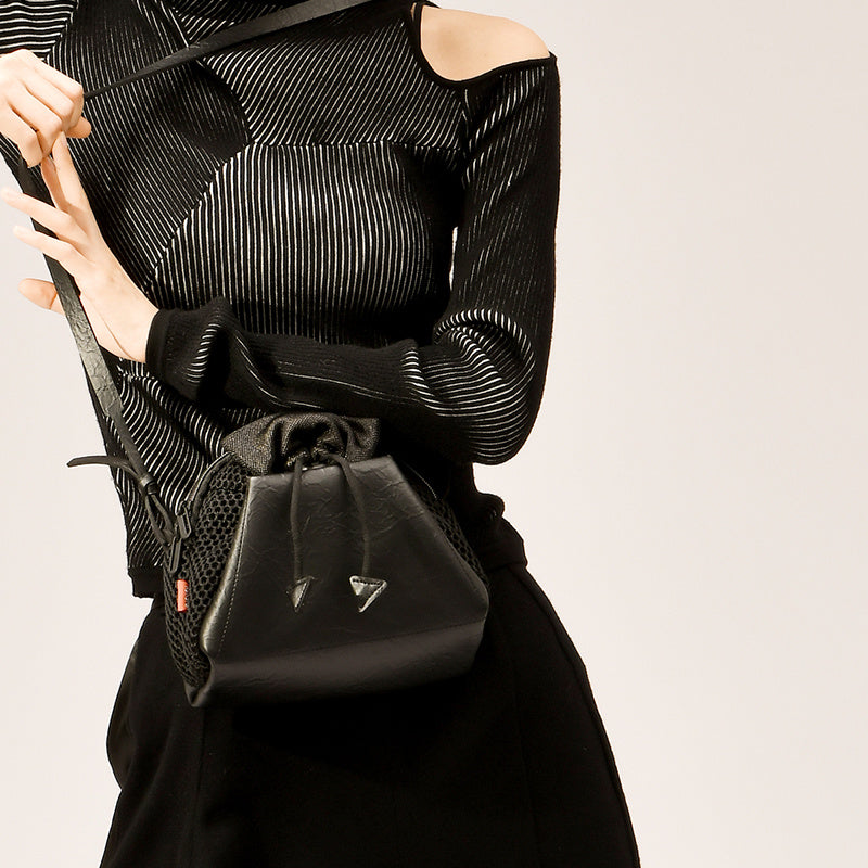 Person holding a black leather handbag against a neutral background