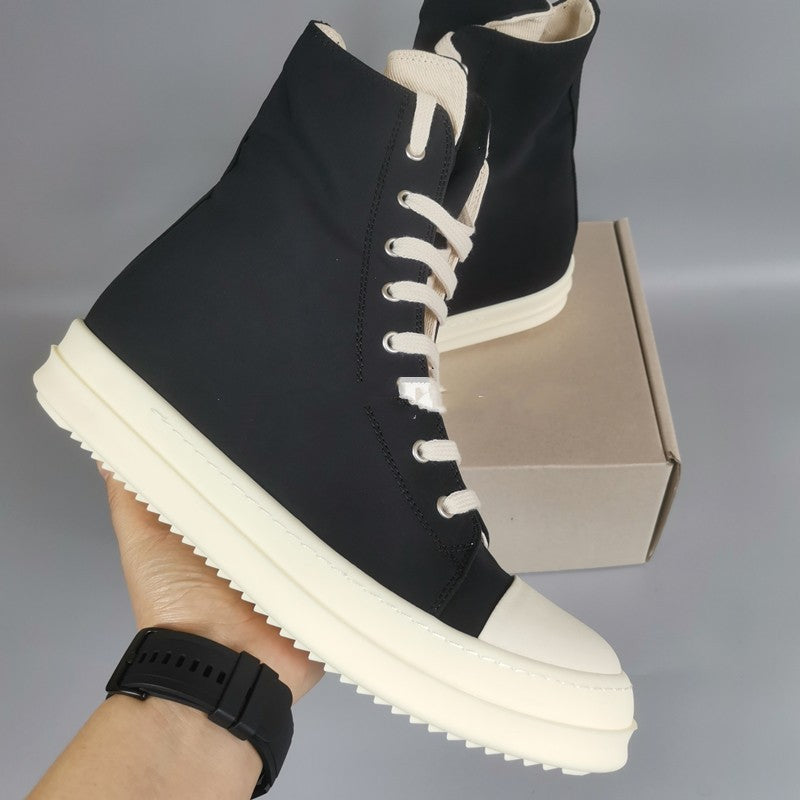 Black high-top sneakers with white soles held by a hand against a gray background