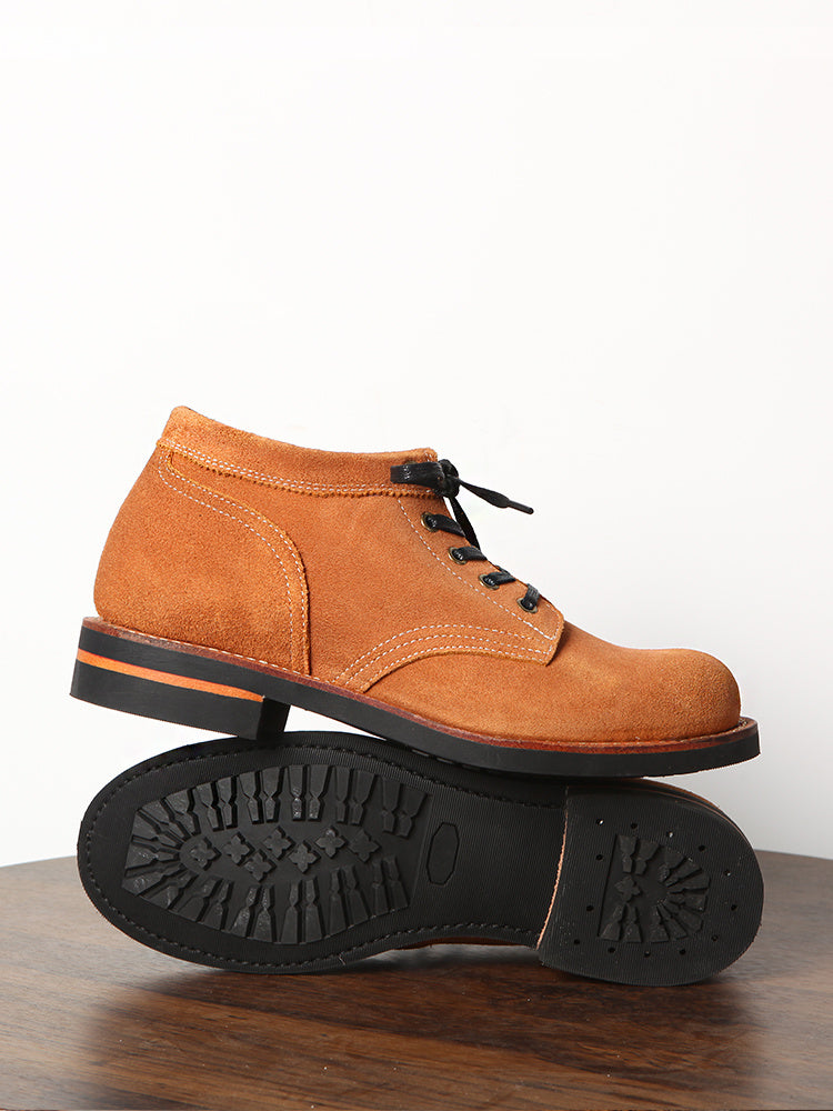 Brown suede shoe with black sole on a wooden surface