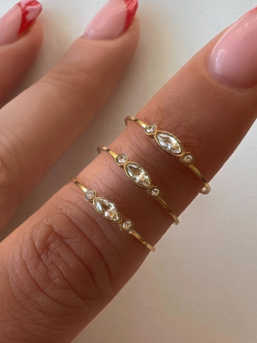 Gold rings with gemstones on a finger against a neutral background