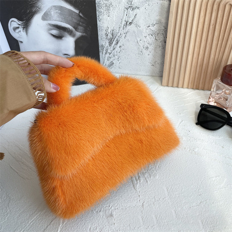 Orange fluffy handbag held by a person on a light surface with a blurred background