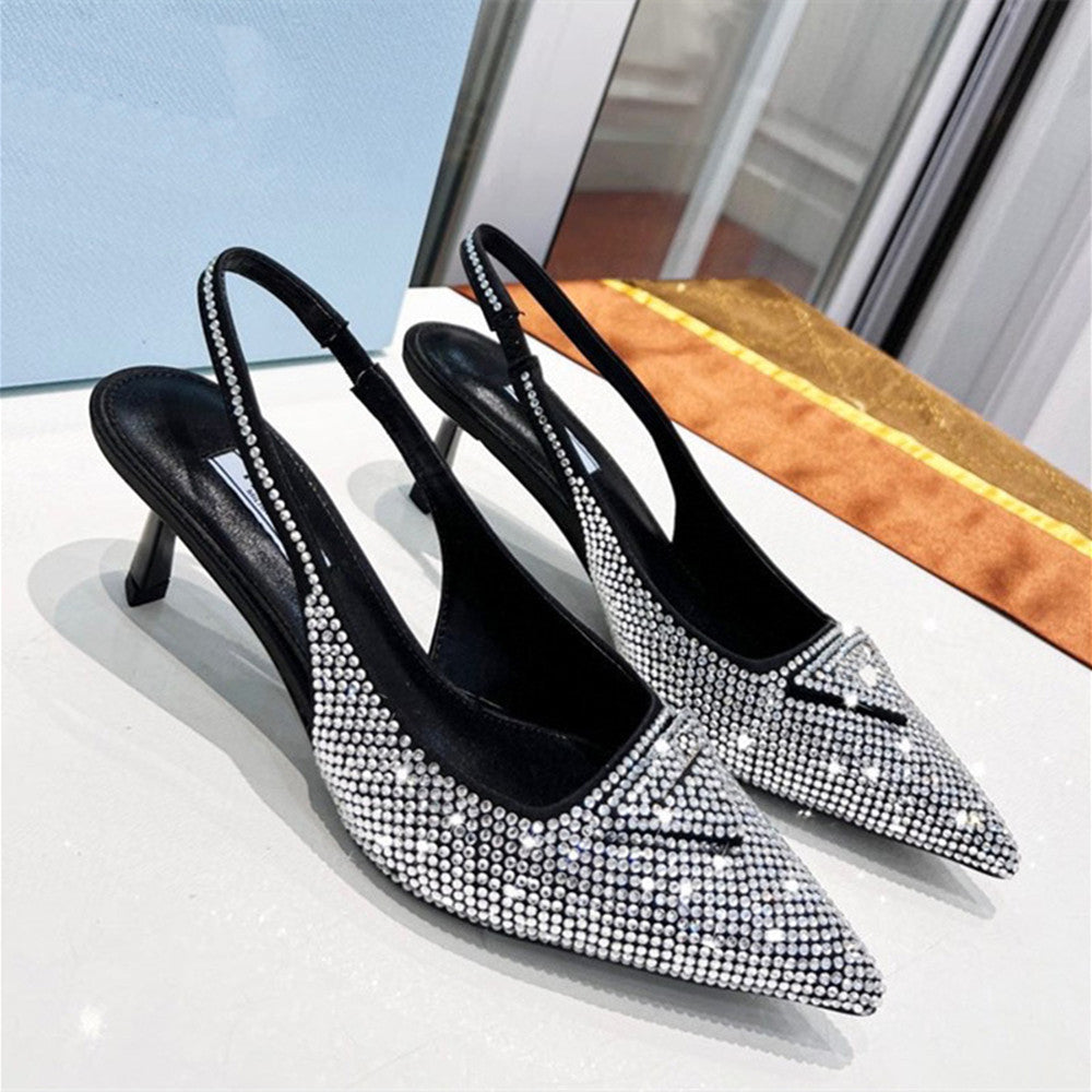 Black high-heeled shoes with silver rhinestone details on a reflective surface.