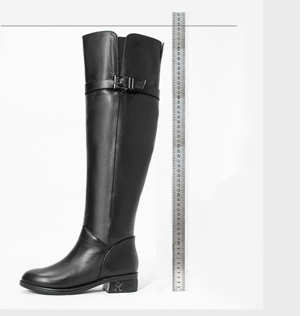 Black knee-high boot with a buckle next to a ruler on a white background