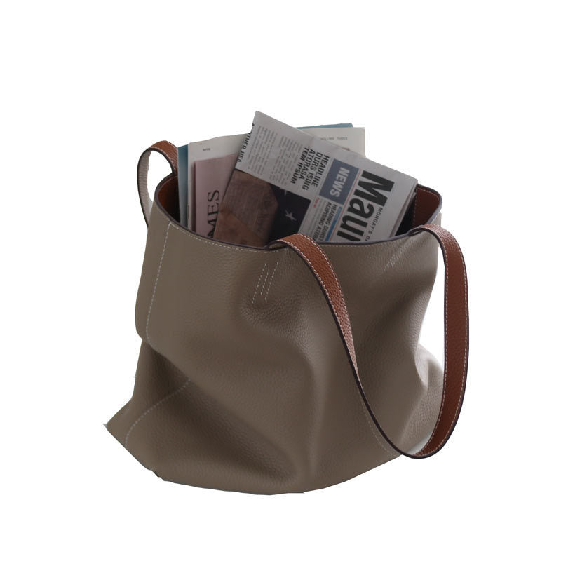 Beige leather bag with brown leather handle and strap, filled with newspapers on a white background