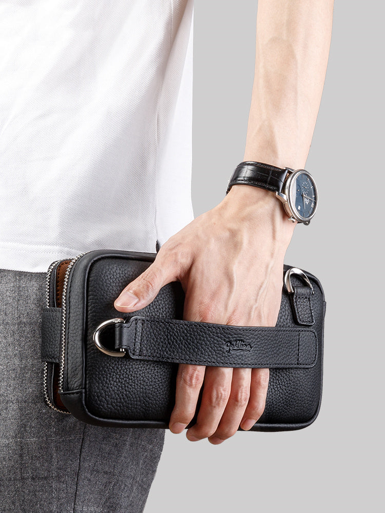 Hand holding a black leather waist bag with a watch on the wrist against a gray background