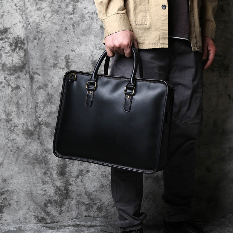 Person holding a black leather briefcase against a textured gray background