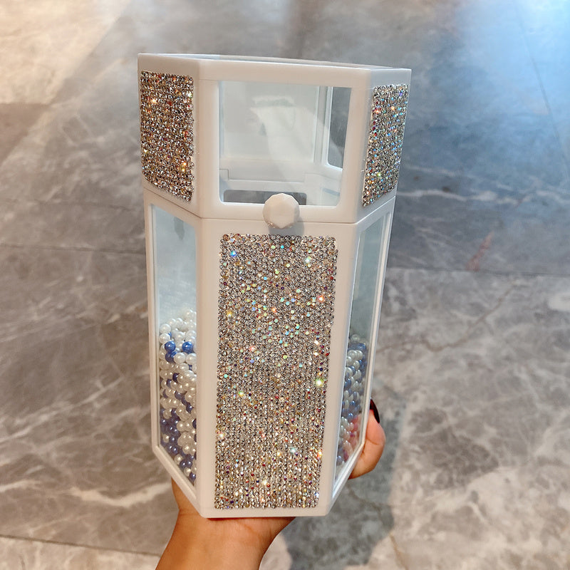 Hexagonal container filled with small beads held by a hand on a marble surface