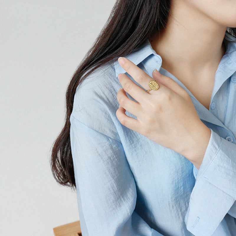Person wearing a gold ring on a light blue shirt against a neutral background