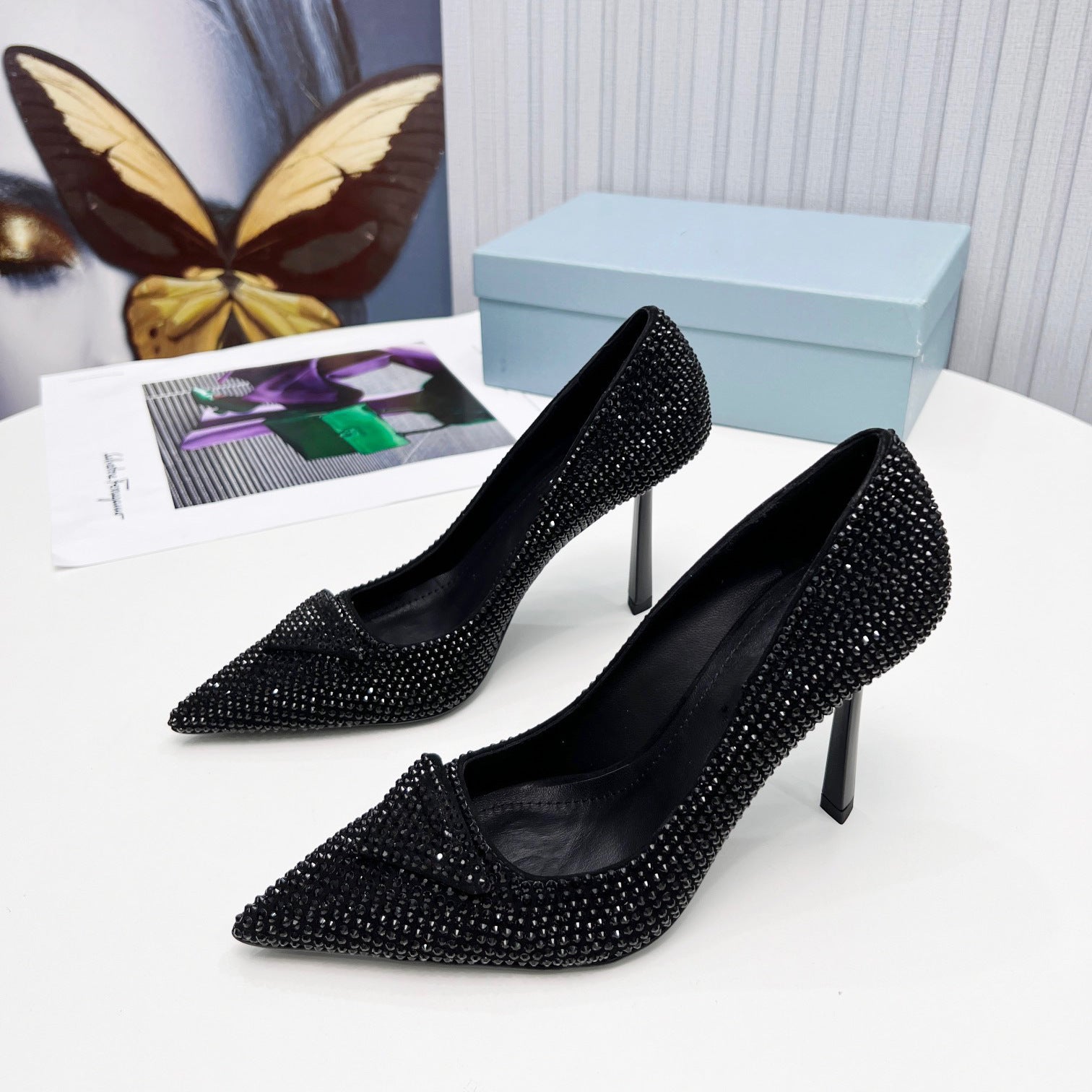 Black studded high-heeled shoes on a white surface with a butterfly and box in the background.