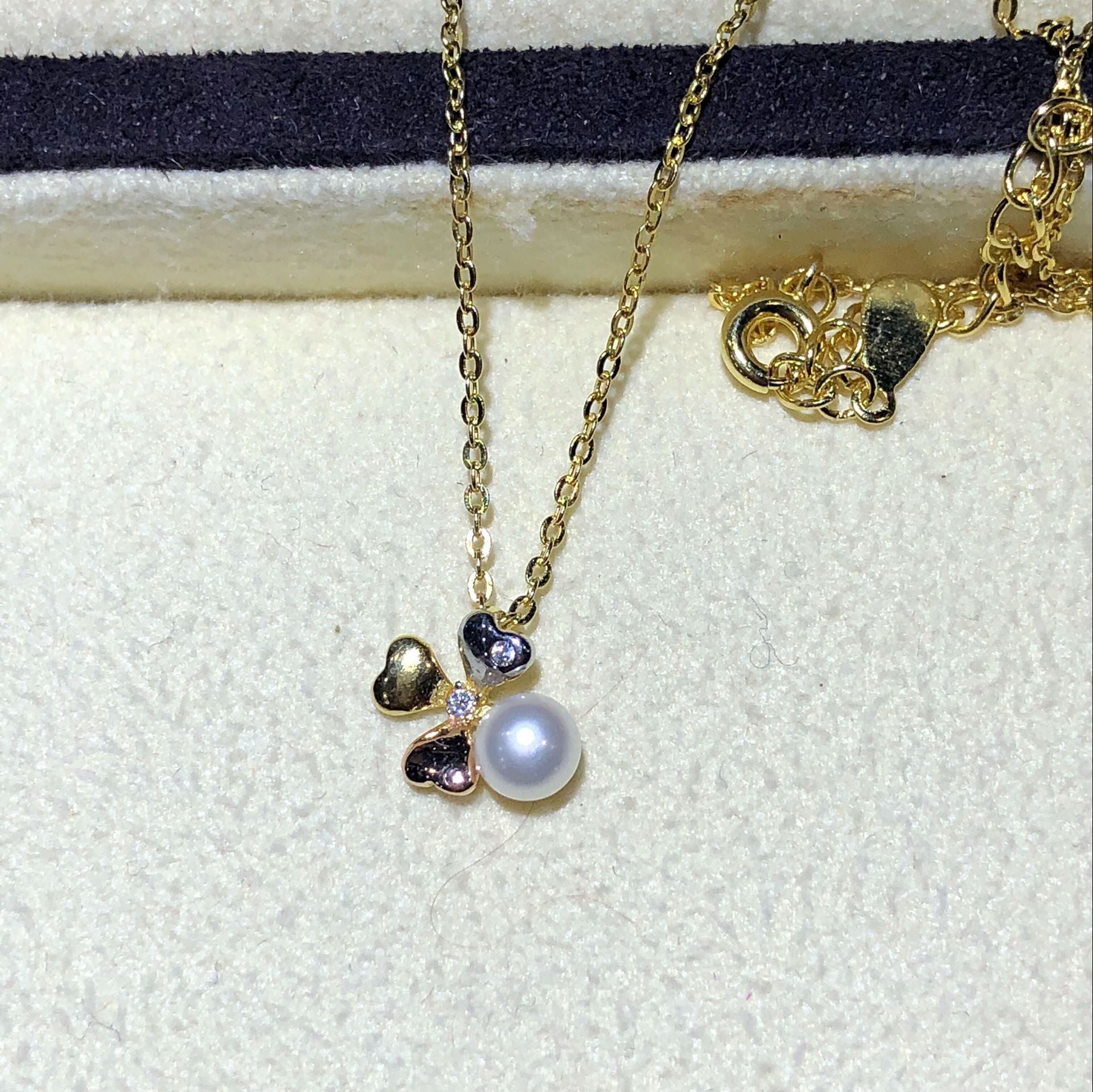Gold necklace with a heart and pearl pendant on a textured white surface
