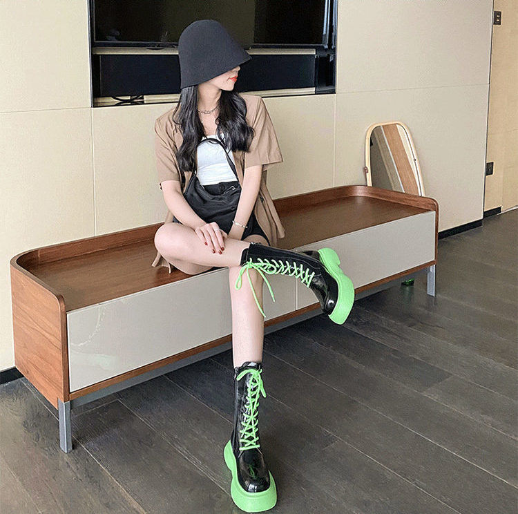 Person wearing black boots with green laces sitting on a wooden bench.