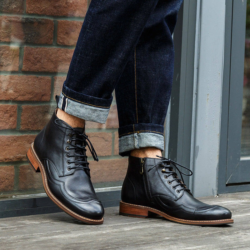 Person wearing black leather boots with brown soles standing on a wooden floor against a brick wall.