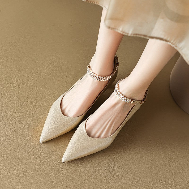 Beige pointed-toe shoes with embellished straps on a beige background