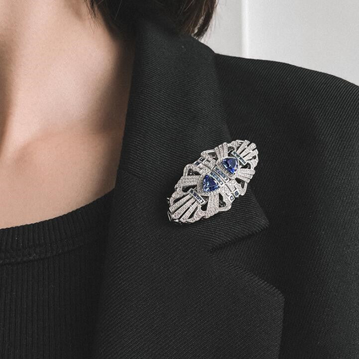 Close-up of a person wearing a black blazer with a decorative brooch featuring blue stones and silver detailing.
