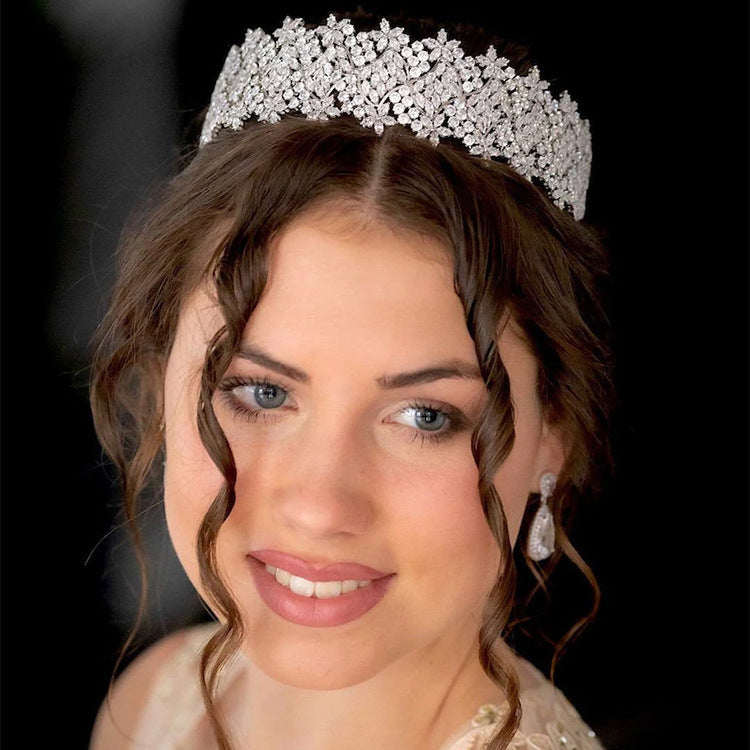 Woman wearing a sparkling tiara and earrings against a black background