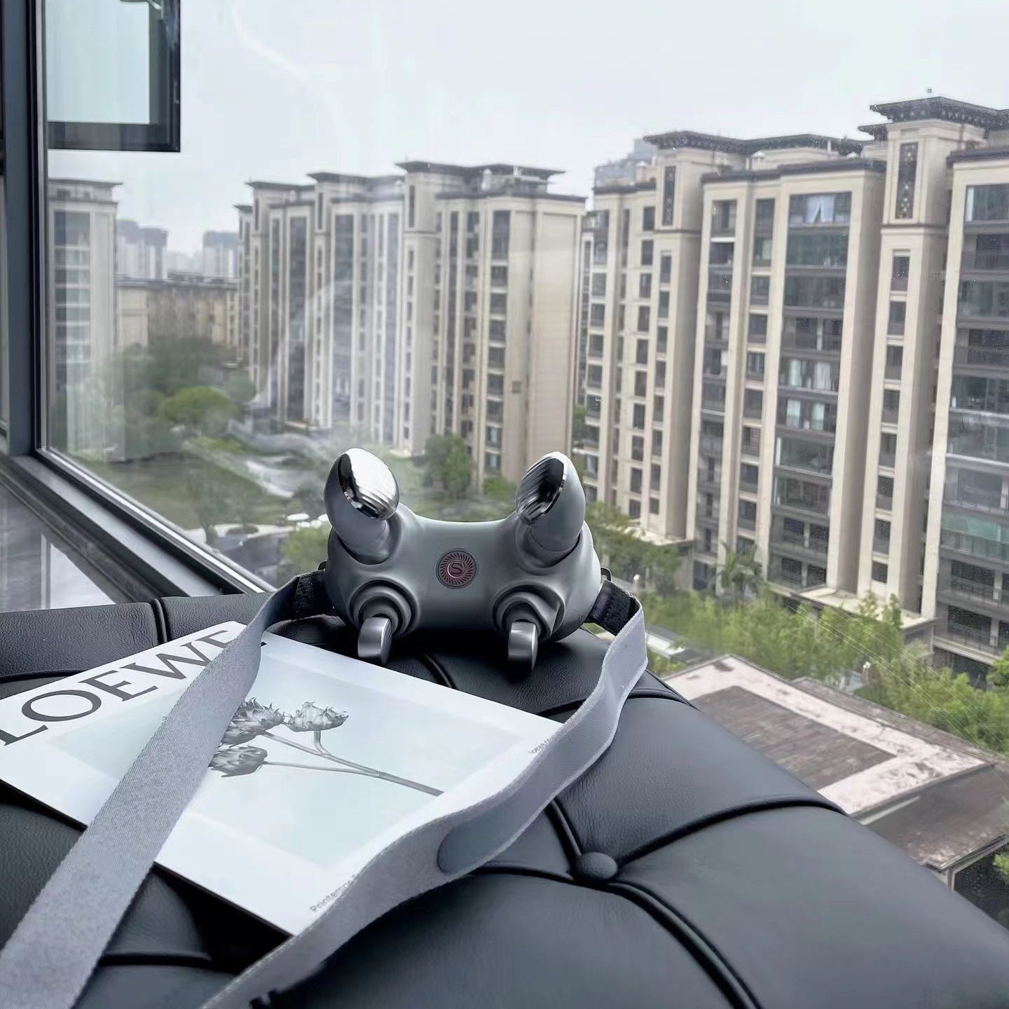 Gray gaming controller on a surface with a cityscape view through a window.